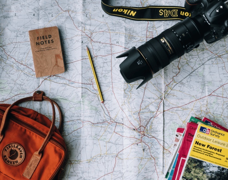 A camera, notebook, and pencil laid out on top of a map.