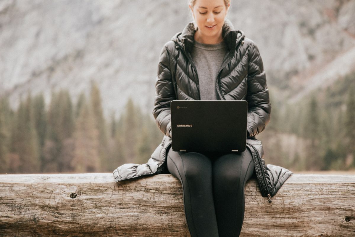 A woman sitting in nature while booking a retreat on a laptop.