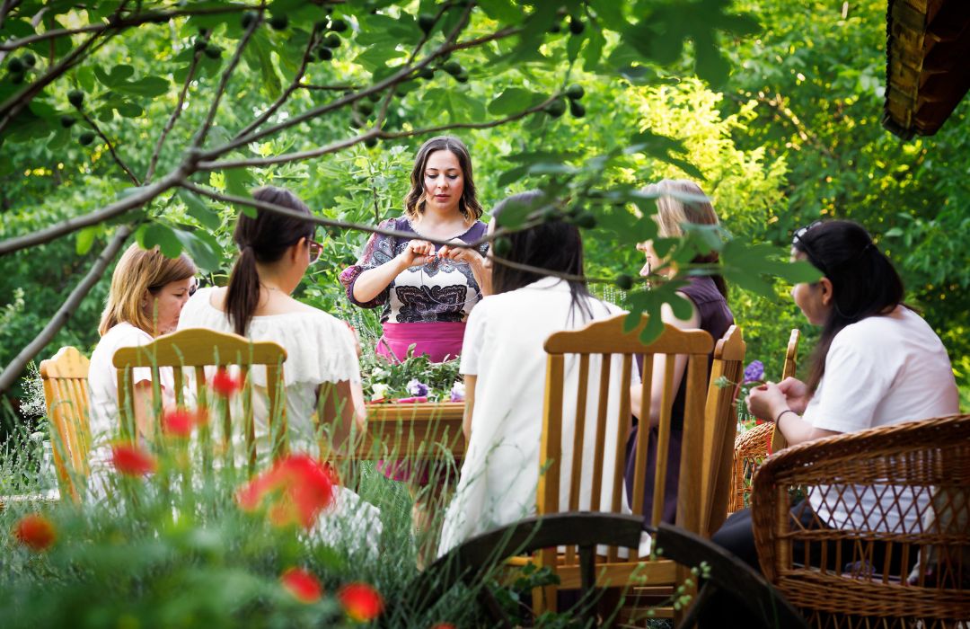 A woman leading a culinary retreat session around a table in a garden.