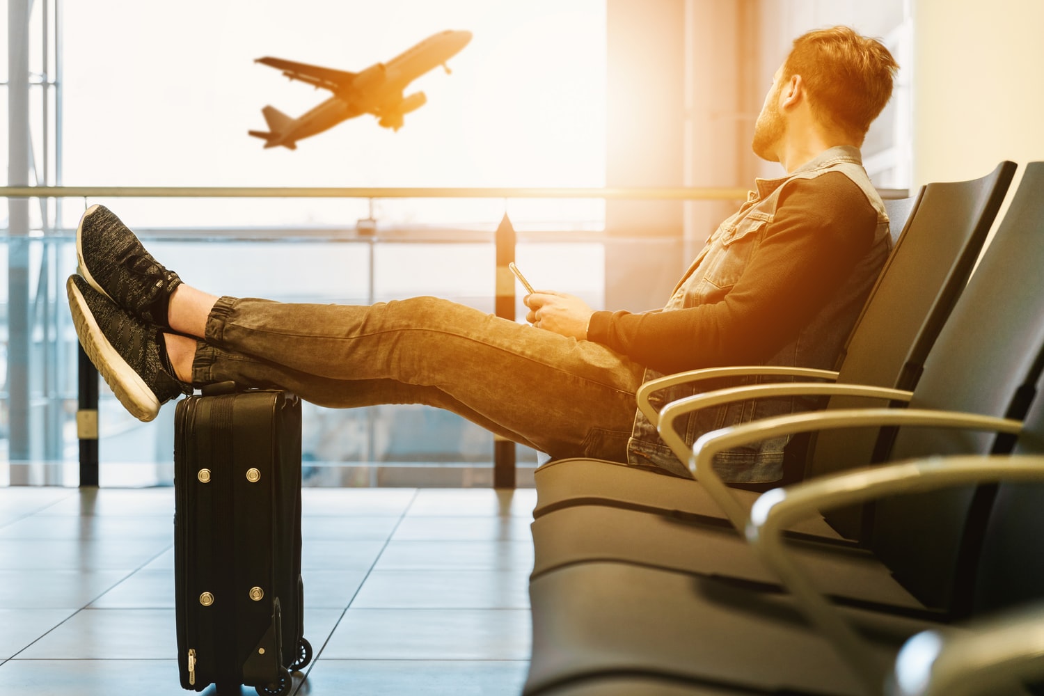 A man sitting at an airport with a place taking off in the background.