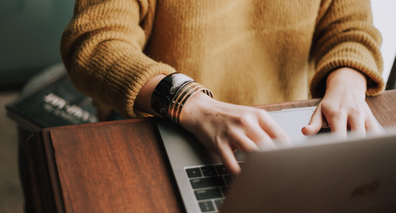 A person in a yellow sweater typing on a laptop.